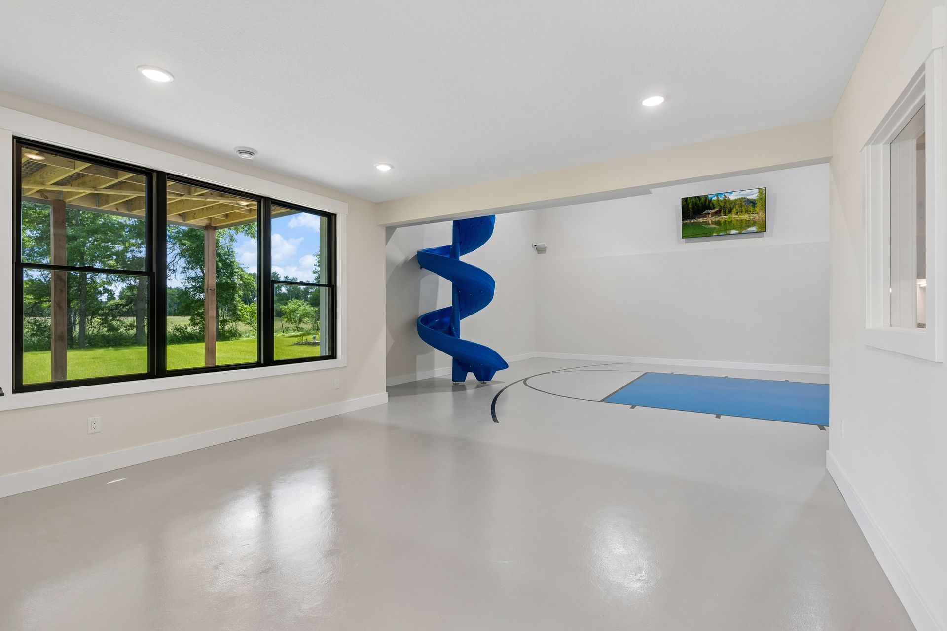 Indoor sport court with basketball hoop, blue slide and large windows